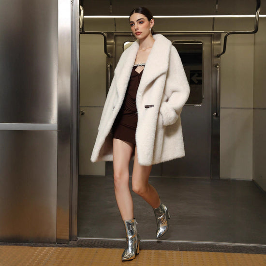 Woman in a white coat and silver boots exiting an elevator.