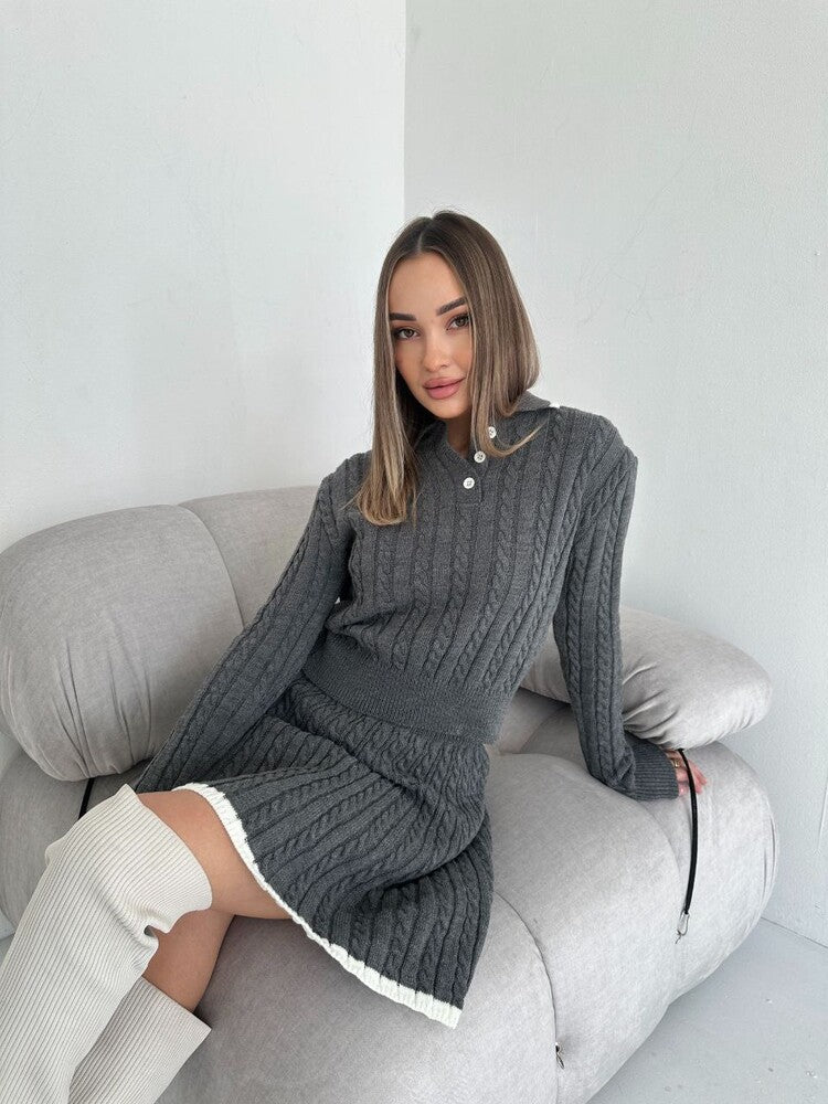 Woman wearing a gray knit dress sitting on a gray couch against a white wall.