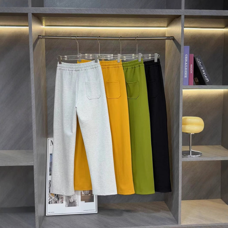 Ralph Lauren Women's Pony Straight Leg Pants. Four pairs of pants in gray, yellow, green, and black hanging on a rack against a gray wall.