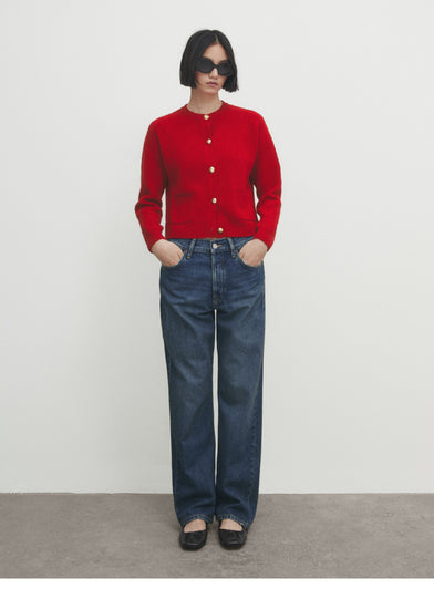 Person wearing a red cardigan and blue jeans on a plain background