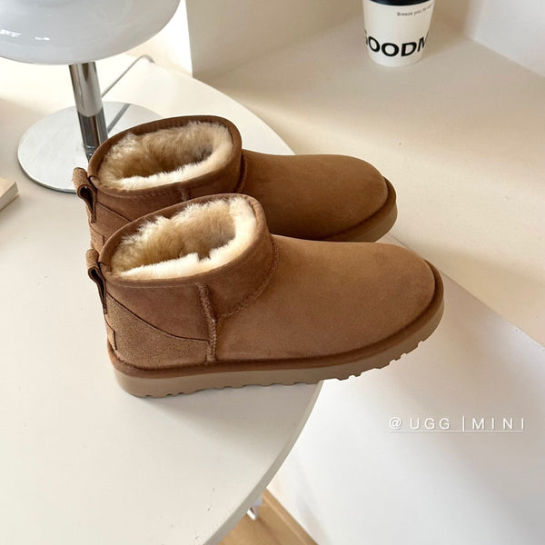 Pair of UGG mini boots on a white surface with 'UGG' branding. UGG Classic Ultra Mini Women's Warm Wool Snow Boots