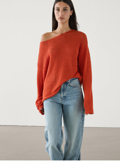 Woman wearing an orange off-shoulder sweater and light blue jeans on a white background