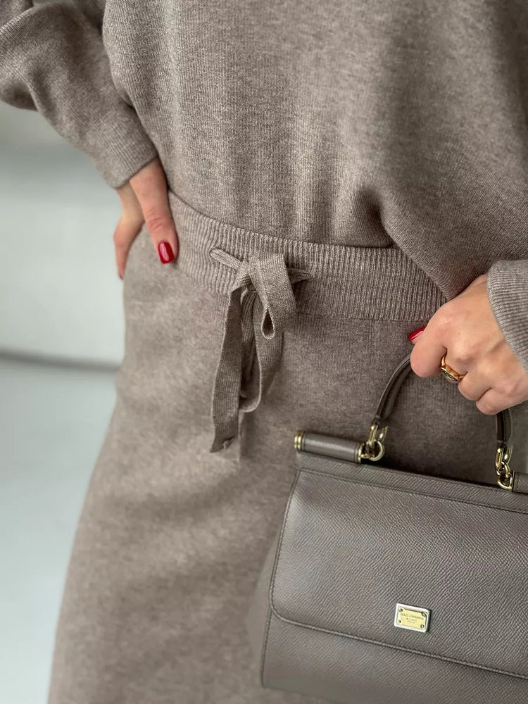 Person wearing a gray outfit holding a matching gray handbag. Chic Elegant Soft Knit Sweater with Skirt Set at Volonka.