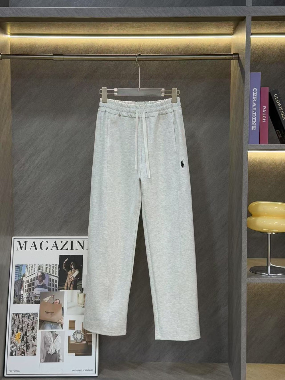 Ralph Lauren Women's Pony Straight Leg Pants. Light gray sweatpants hanging on a rack with a magazine and chair in the background.