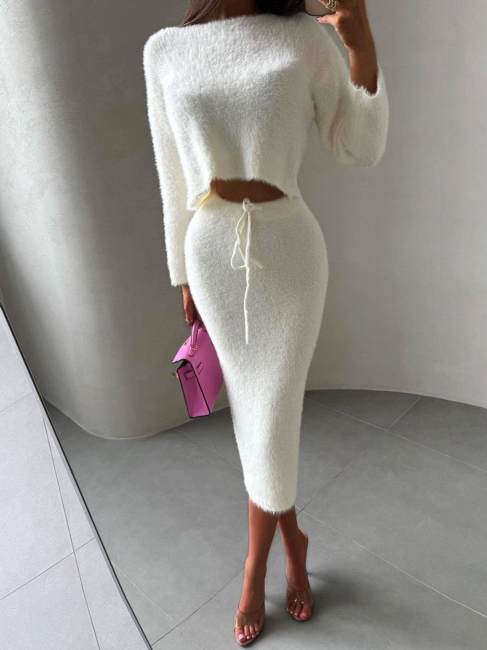 Woman wearing a white knit outfit with a pink handbag in a minimalistic setting, Luxury Fuzzy Knit Two Piece Skirt Set Chic Celebrity Style at Volonka.