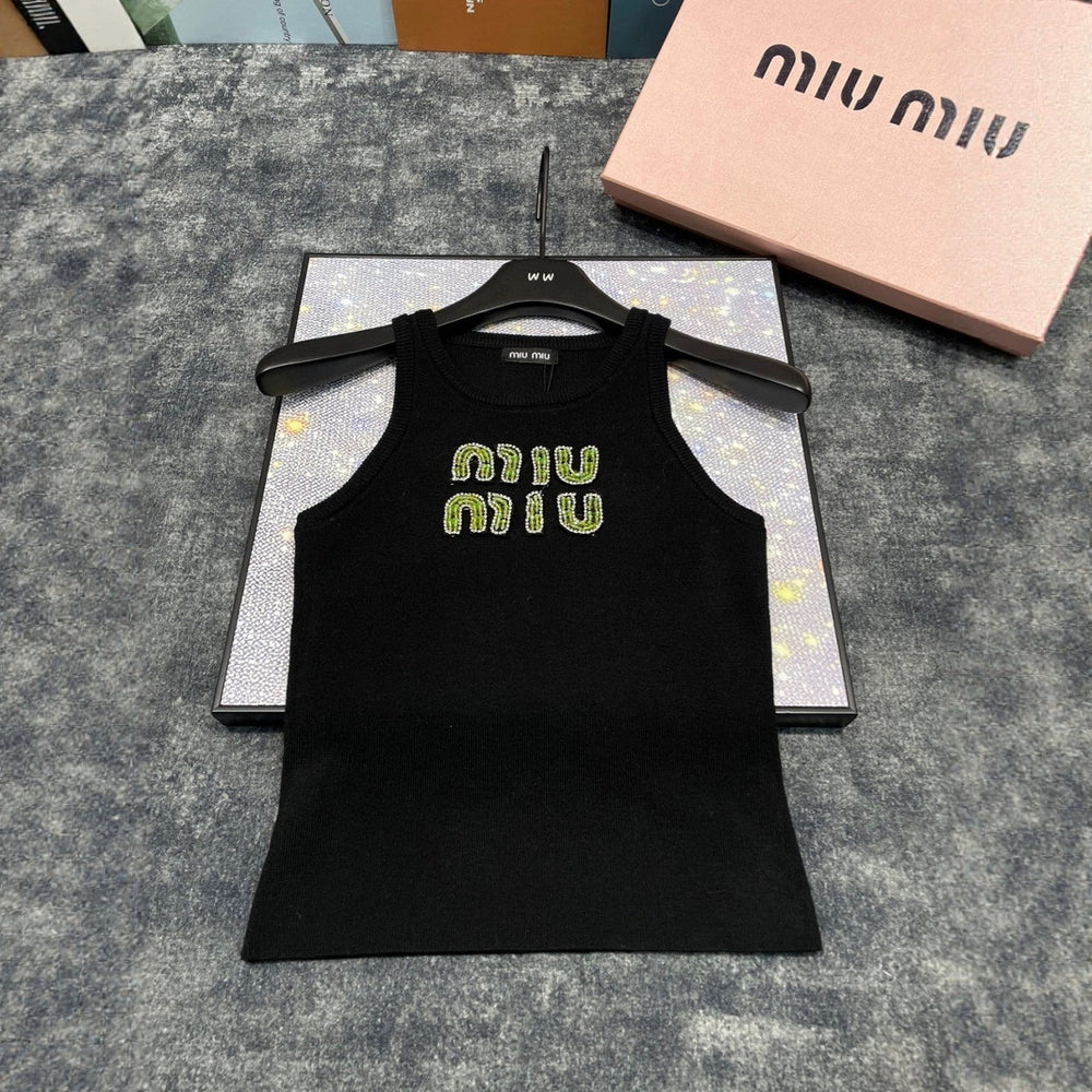 Black tank top with 'MIU MIU' embroidery on a hanger with a pink box in the background.