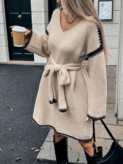 Woman in a beige sweater dress with black trim holding a coffee cup outdoors. Womens Knit V-Neck Midi Dress Tie-Waist Loose Autumn Style at Volonka.