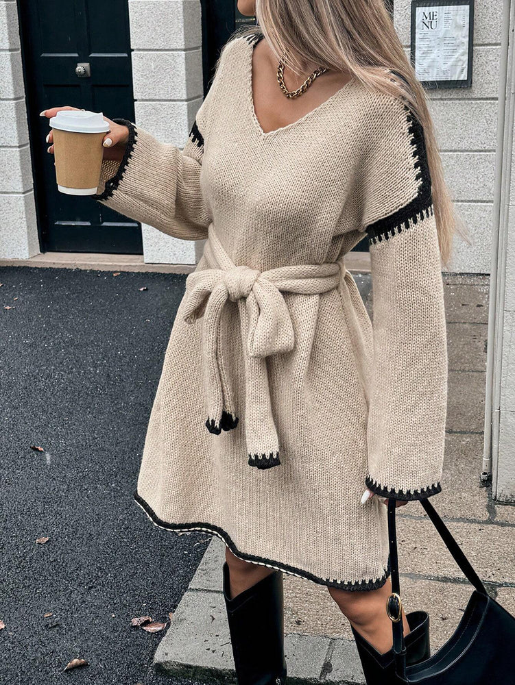 Woman in a beige sweater dress with black trim holding a coffee cup outdoors. Womens Knit V-Neck Midi Dress Tie-Waist Loose Autumn Style at Volonka.