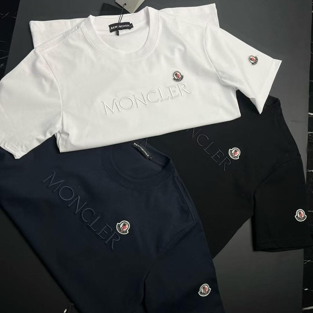 White and black Moncler shirts with brand logo on a dark surface