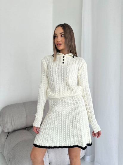 Woman wearing a white cable knit dress with black trim in a minimalistic room.