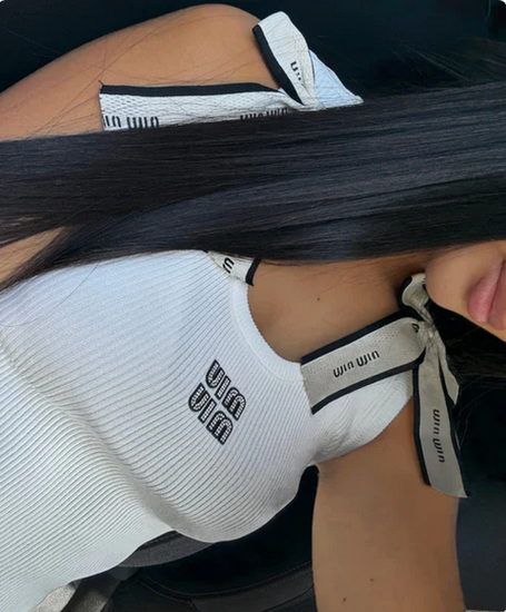 woman wearing a white sleeveless top with brand logos, sitting on a black chair.with knot