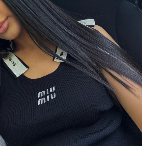 woman wearing a premium black chic top with 'MIU MIU' branding, sitting in a car. 