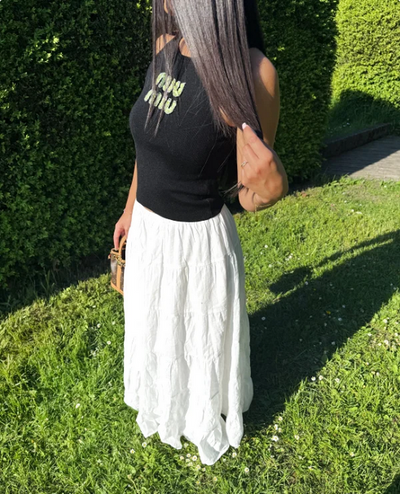 woman wearing a black top with text and a white skirt standing on grass. MIUMIU premium stylish ribbed jersey top