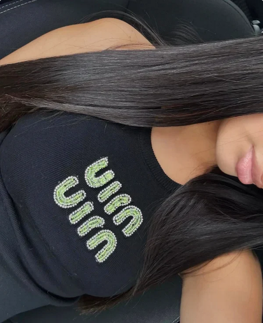 woman holding long dark hair with a black chair with 'MIUMIU' branding in the background