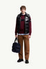 Man wearing Moncler unisex Bormes down vest jacket, black puffer vest over a red sweater, holding a black bag.
