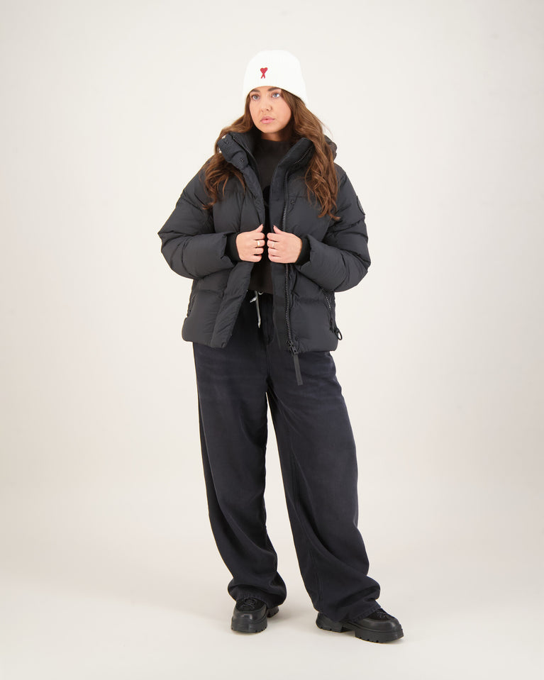 Woman wearing a dark gray winter coat, black pants. Canada Goose Junction Parka Black Label Unisex Winter Jacket