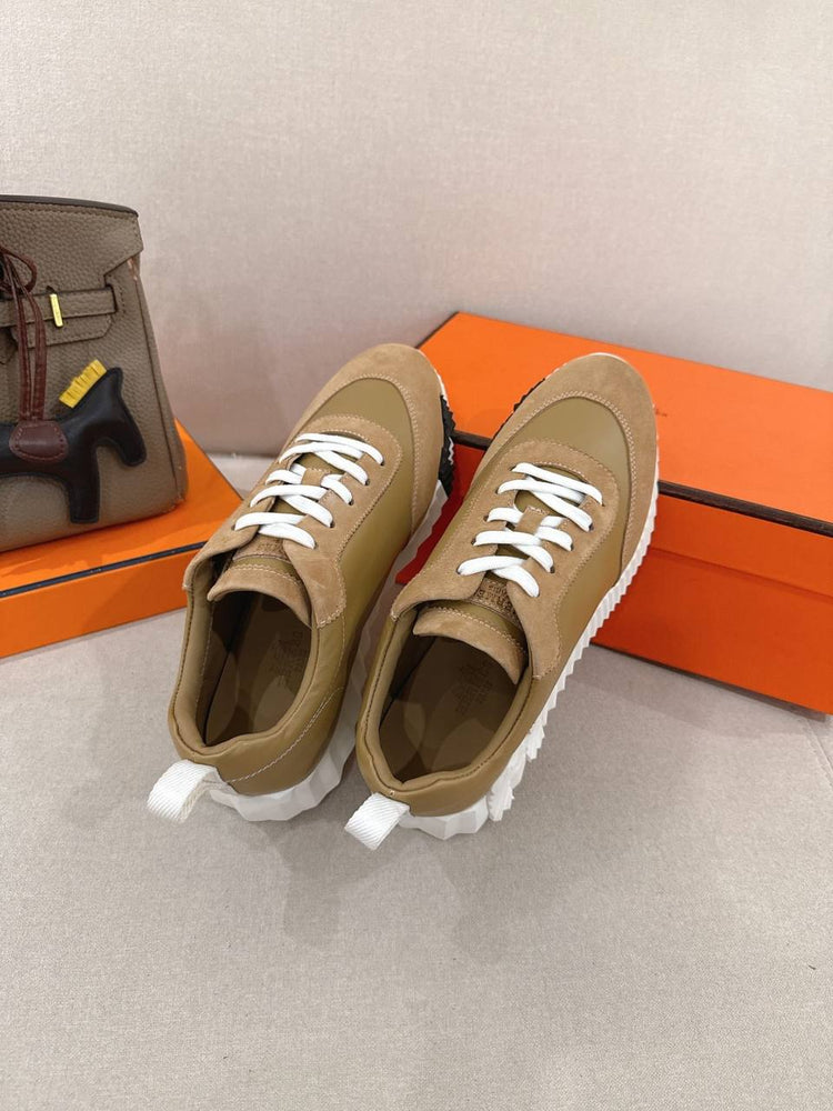 Hermes Unisex Bouncing Sneakers displayed with orange boxes and a designer handbag in the background.