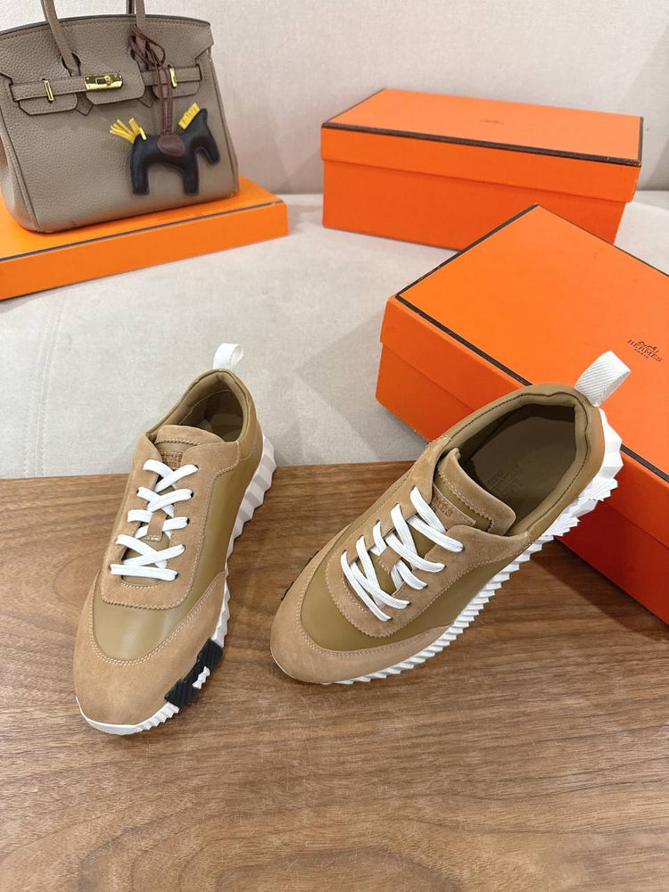 Hermes Unisex Bouncing Sneakers displayed with orange boxes and a designer handbag in the background.
