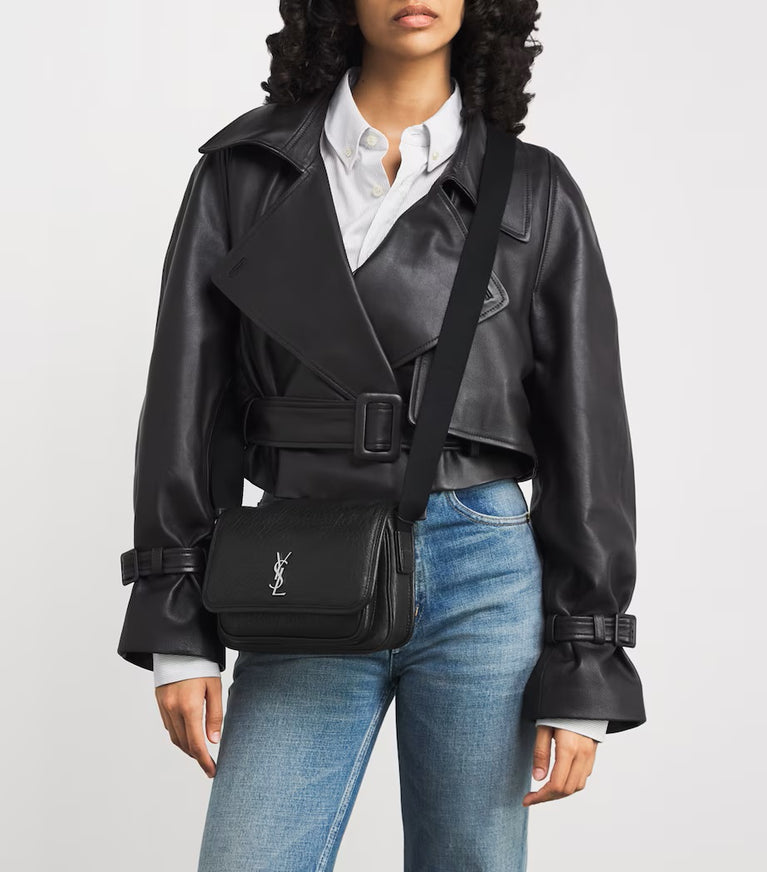 Person wearing a black leather jacket and blue jeans, carrying a black YSL bag. Saint Laurent Niki Small leather messenger bag at Volonka.